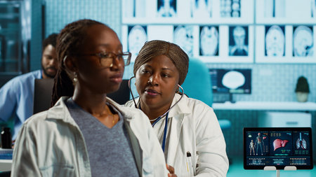 African american female medic does a respiratory consultation with stethoscope, listening to heartbeat and lungs functioning normally. Doctor checking pulse for her young patient. Camera A.の写真素材