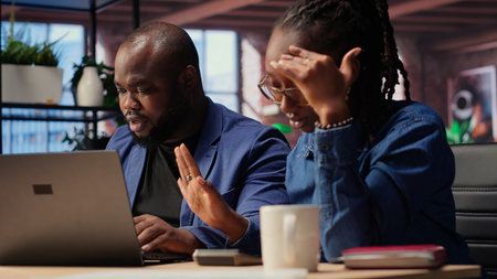 Worried African American woman looks at tax numbers on documents while her partner reassures her,...