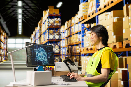 Asian warehouse clerk using AI brain systems with neural networks, using virtual assistant to process orders and ensure express delivery. Updating the tracking software on computer.の写真素材