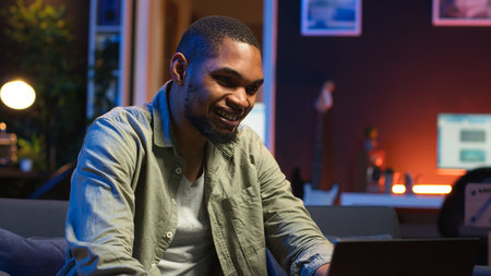 African american person being happy and proud with his project achievement, accomplishing multiple freelancing tasks at home. Young adult in the living room cheering. Camera B.の写真素材