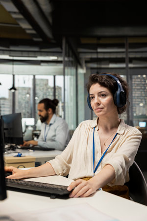 Female executive assistant listening to songs on headphones at the workstation, managing...