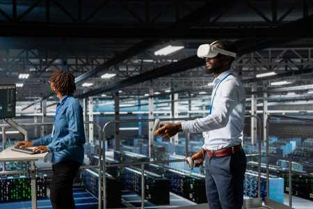Black male IT expert uses VR glasses on industrial platform in server room, using high tech tools to manage machine learning for automation. Neural network systems in a data center.の写真素材