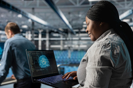 Smiling IT expert in server room using laptop to improve AI system scalability for increased...