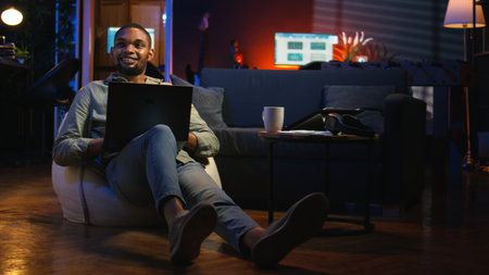 Guy checking financial balance and working on accounting analysis, ensuring revenue growth at home. African american worker enjoys remote job using statistics. Camera A.の写真素材