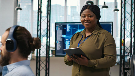 Smiling female engineer next to office coworkers developing software applications, integrating AI...