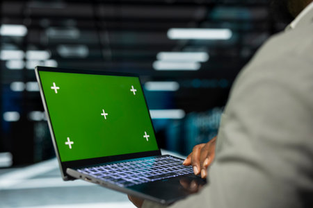 Close up of engineer in data center using isolated screen laptop to check for server performance issues. IT professional in server hub fixing errors slowing down hardware using mockup notebookの写真素材