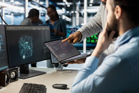 Close up of data center admins monitoring system performance using laptop, identifying bottlenecks....