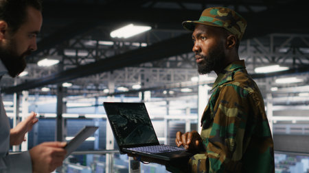 Military technician in data center monitoring warfare drone telemetry on laptop dashboard. IT specialist in army server room using tactical interface on notebook to support aerial operationsの写真素材