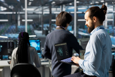 Engineer using laptop in data center with gear managing AI training datasets. IT expert using...
