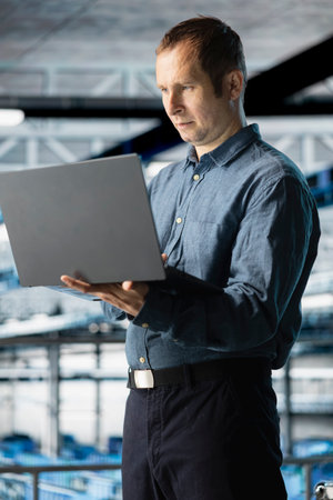 Engineer in data center refining algorithms on laptop for faster processing. Employee in server farm writing code for infrastructure resource optimization using notebook deviceの写真素材