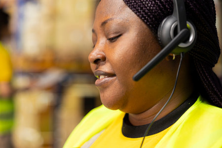 Close up of female support team answering help line calls in a storage room, assisting with package...