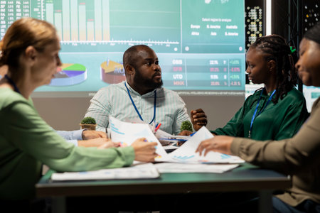 Diverse employees discuss project details and forecast information at night, ensuring business...
