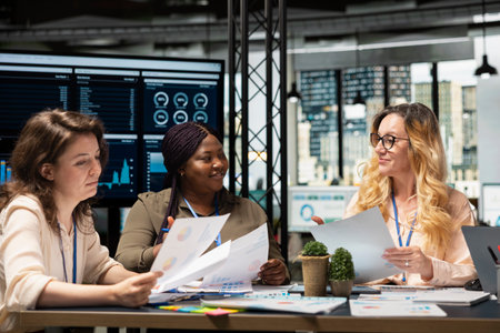 Diverse company associates express ambition and determination, briefing session to align vision with project goals and review finance reports on the table. Corporate feminism in organization.の写真素材