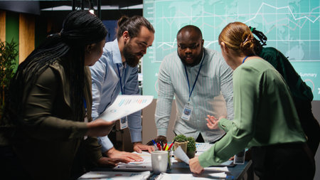 Multiethnic team exchanging files and review forecasting diagrams at night, meeting in a quiet...