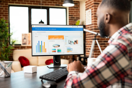 Black businessman looking at desktop monitor, studying company financial documents at home office. Remote worker analyzes business performance and prepares strategic growth plans for startup success.の写真素材