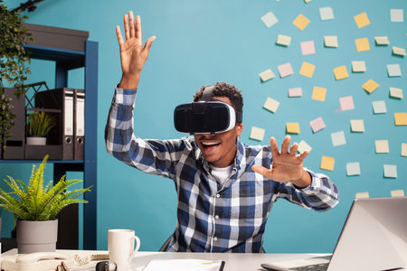 Excited employee uses VR headset, blending technology with workplace creativity. African american...