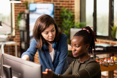 Caucasian manager attentively listening as black woman shares progress updates, gesturing to...
