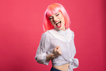 Joyful caucasian lady expressing excitement with mouth open and fist raised, standing isolated over pink background. Beautiful happy woman filled with enthusiasm, celebrating good news and success.の写真素材