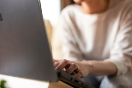 Selective focus on fingers of female remote worker typing on laptop keyboard. Closeup of woman...