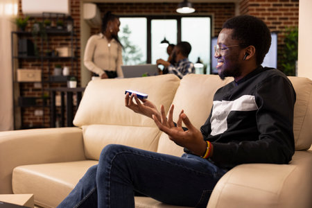 African american male entrepreneur wearing earphones using holographic interface while discussing...