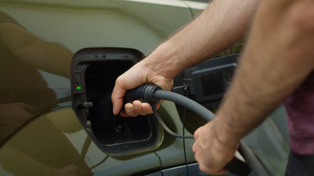 Close up of eco conscious driver opening charging port flap of electric car to recharge, supporting...