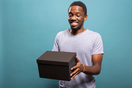 African american man carries a carton, enjoying the moment of receiving and unboxing a parcel. Smiling black male individual holding a cardboard box from a postal delivery service.の写真素材
