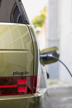 Close up of red tail light and plug in badge on electric vehicle charging at public station. Electric car plugged into charger, reducing greenhouse gas emissions, sustainable transport conceptの写真素材