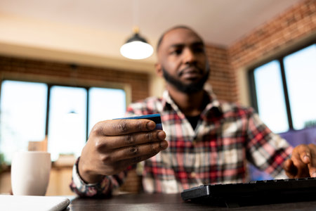 African american businessman typing on keyboard, completing booking reservation by inputting credit card details. Selective focus on black male freelancer making online payments on desktop pc.の写真素材