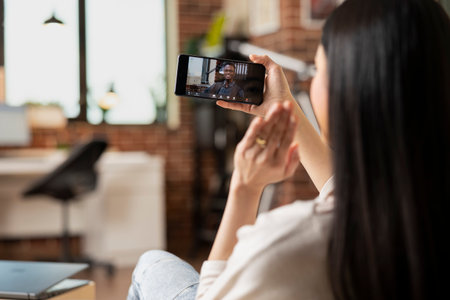 Female freelancer waving hello to african american client during virtual meeting on mobile phone. Businesswoman and black businessman brainstorm online during remote video conference.の写真素材