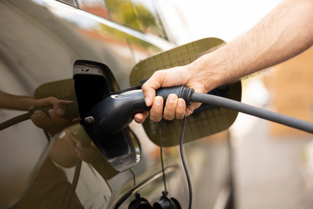 Close up of man opening vehicle inlet port of EV automobile to refill it using green electricity. Driver attaching electric cable connector to electric SUV car to recharge battery before tripの写真素材