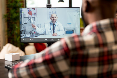 Self employed man sits at desk using computer for video call with caucasian general physician....