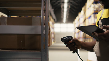 Young man using scanner on boxes barcodes tags in fulfillment center. Organized shelving, package labels and route planning support efficient distribution and shipment. Logistics hub. Camera A.の写真素材
