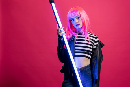 Caucasian female model stands in dramatic lighting, gripping vertical LED stick. Beautiful woman...