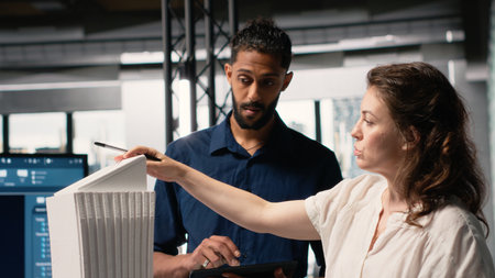 Multiethnic real estate team evaluate a residential project with 3D models and architectural software, respecting zoning regulations for the property. Blueprints and city planning tools.の写真素材