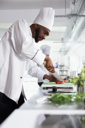 Precision and technique shine as a chef chopping fresh veggies on a cutting board. Modern kitchen where an expert is slicing and preparing vegetables for a new fine dining meal at the stove.の写真素材