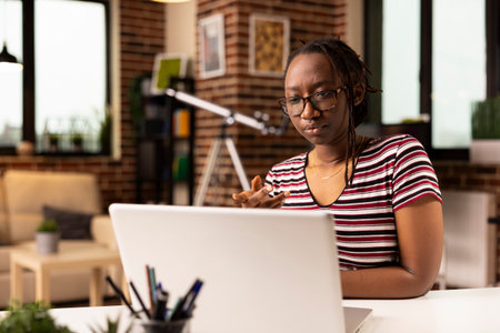 Focused black woman speaking with team during virtual meeting on laptop. African american female employee working from home, participating in video conference with coworkers on personal computer.の写真素材