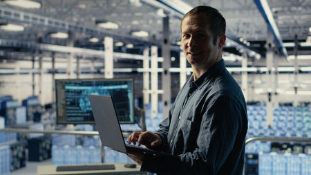 Engineer in data center checks AI dashboard using laptop during routine systems review. IT expert...
