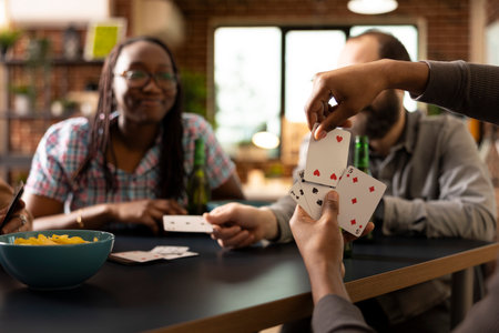 Closeup of african american individual making his move during indoor gaming session with close friends. Hand of black male person holding cards and playing with multiethnic companions.の写真素材