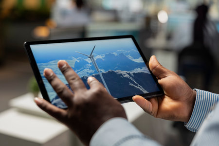 Close up of engineer in office using tablet to analyzes wind turbine and improve renewable energy efficiency. RD professional uses CAD app on device to upgrade windmill, boosting clean energy outputの写真素材