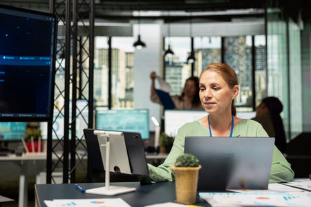 Female entrepreneur works with neural networks for analytics, AI automation algorithms on TV monitor next to desk. Artificial intelligence helps with decision making in a corporate office.の写真素材