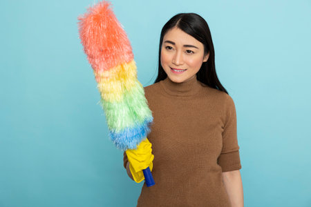 Cheerful housekeeper wearing rubber gloves posing with colorful duster, ready to clean. Smiling...