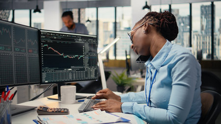 Equity analyst in office reviews quarterly earnings paperwork to assess future stock market value, talking on phone. Trader making calls, conducting financial analysis to improve investmentsの写真素材