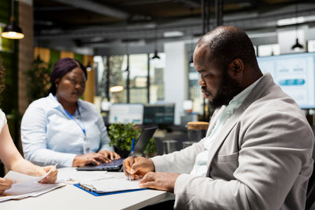 Black confident man signing legal paperwork with the HR manager and beginning the onboarding journey, confirming the approval of the job application. Exciting business position.の写真素材