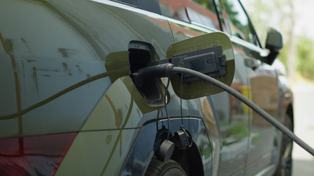 Eco friendly electric car battery being recharged, concept of transition to alternative energy transportation. Charging station electric cable connector attached to EV vehicle, handheld camera shotの写真素材