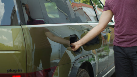 Close up of man closing vehicle inlet port of EV eco friendly SUV car after charging it. Driver closes charging port flap of alternative energy based electric vehicle after finishing refillの写真素材