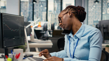 Equity analyst in office reviews quarterly earnings paperwork to assess future stock market value, talking on phone. Trader making calls, conducting financial analysis to improve investmentsの写真素材