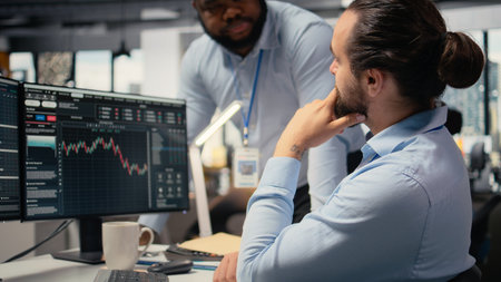 Coworkers collaborate on trading strategies in office, reviewing stock market data together. Team of...