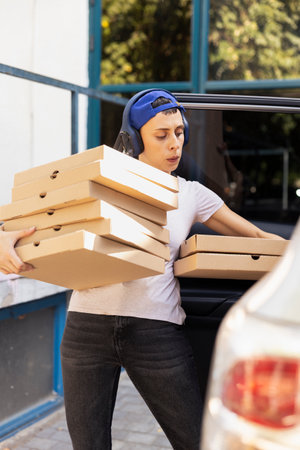 Takeaway delivery worker parking the car and bringing pizza boxes to client at the front door, delivering a massive fast food order. Female courier ensuring an express five star service.の写真素材