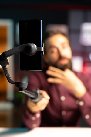 Focus on mobile phone used by media star in blurry background hosting online show in neon lit studio, shooting vlog. Close up shot of cellphone used by man during streaming service broadcastの写真素材