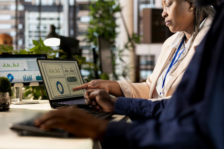 African american staff gathers and examines monthly revenue balance at desk, planning next steps in financial operations to guarantee success. Workers team reviewing performance data.の写真素材